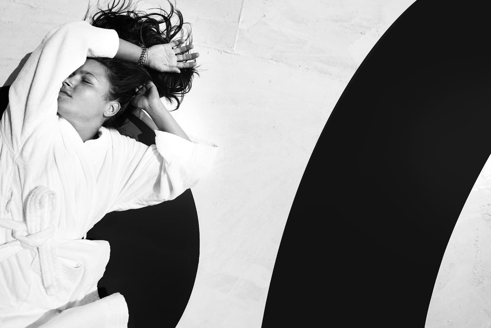 Editorial black-and-white portrait of a woman in a spa robe against sculpted archway walls